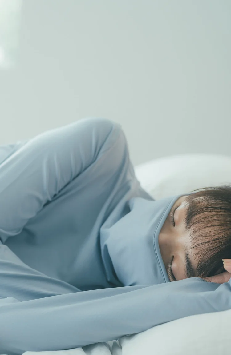 ブルーのリカバリーウェアを着てベッドで眠る女性